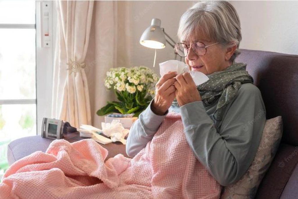 mulher idosa sentada na cama doente assoando seu nariz